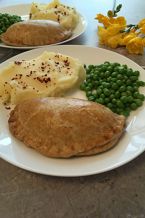 two plates of Cornish Pasties with mash potatoes and peas